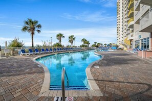 Piscina com cadeiras de praia azuis e palmeiras ao fundo.
