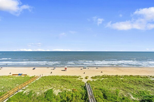 A beach with a wooden boardwalk leading to the shore, sandy beach, and the ocean.