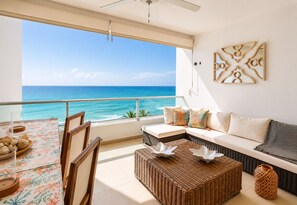 Un balcone con vista sull'oceano, un divano in vimini, un tavolo da pranzo con tovaglia floreale e una ventola a soffitto.