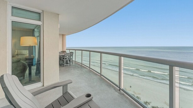 A balcony with a view of the ocean, a table with chairs, and a lamp. - Spacious 3 bedroom unit in Bluewater Keyes | Bluewater Keyes - 1105 (North Myrtle Beach)