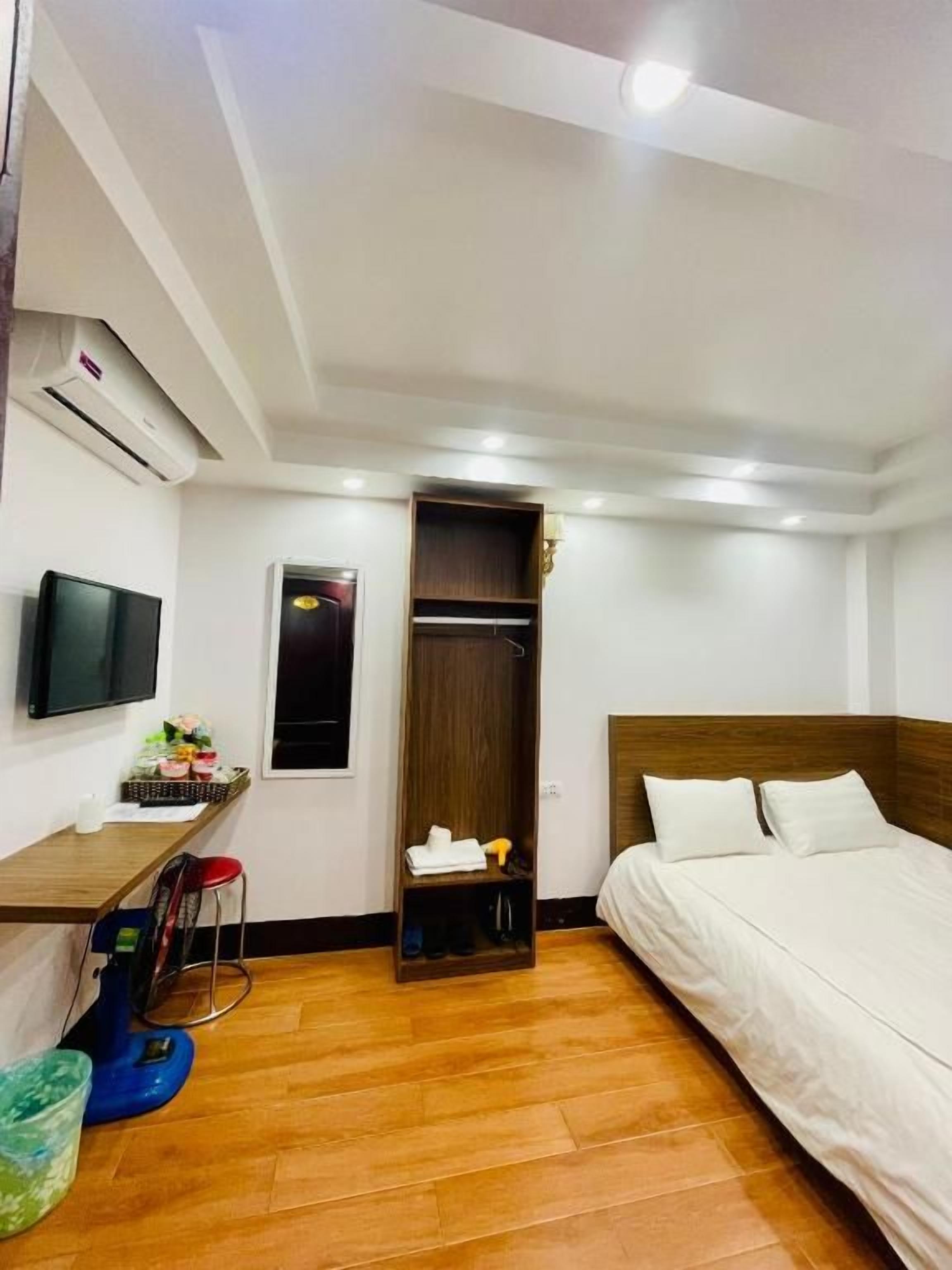 A hotel room with a bed, a desk with a chair, a television, an air conditioning unit, and a wardrobe.