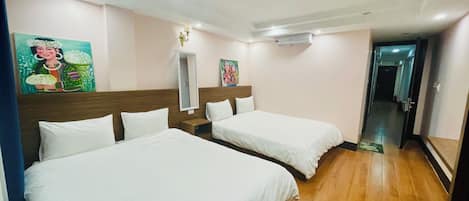 A hotel room with two beds, a wooden floor, a mirror, and artwork on the walls.