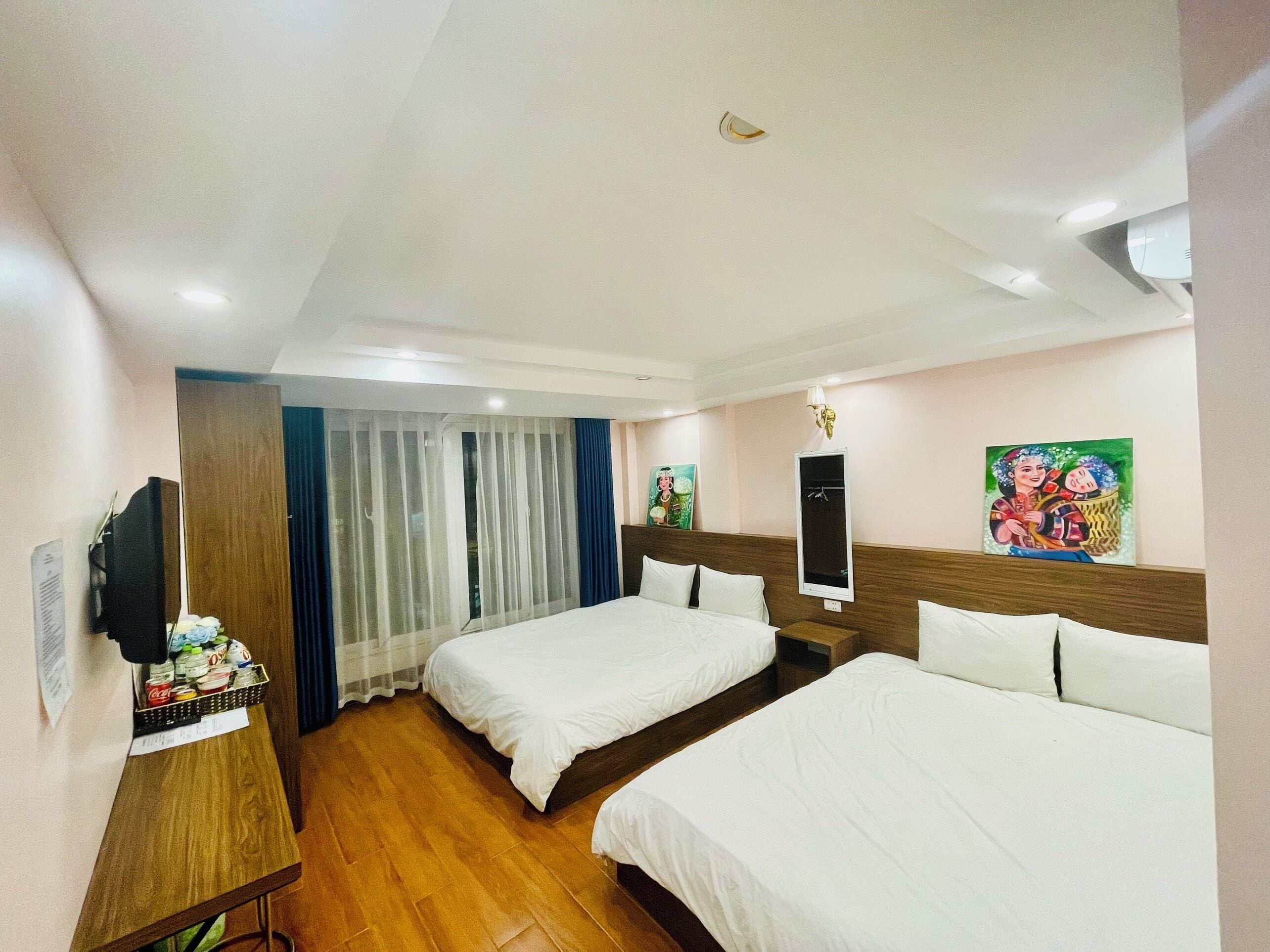 Habitación de hotel con dos camas, un escritorio de madera, un televisor y un cuadro en la pared.