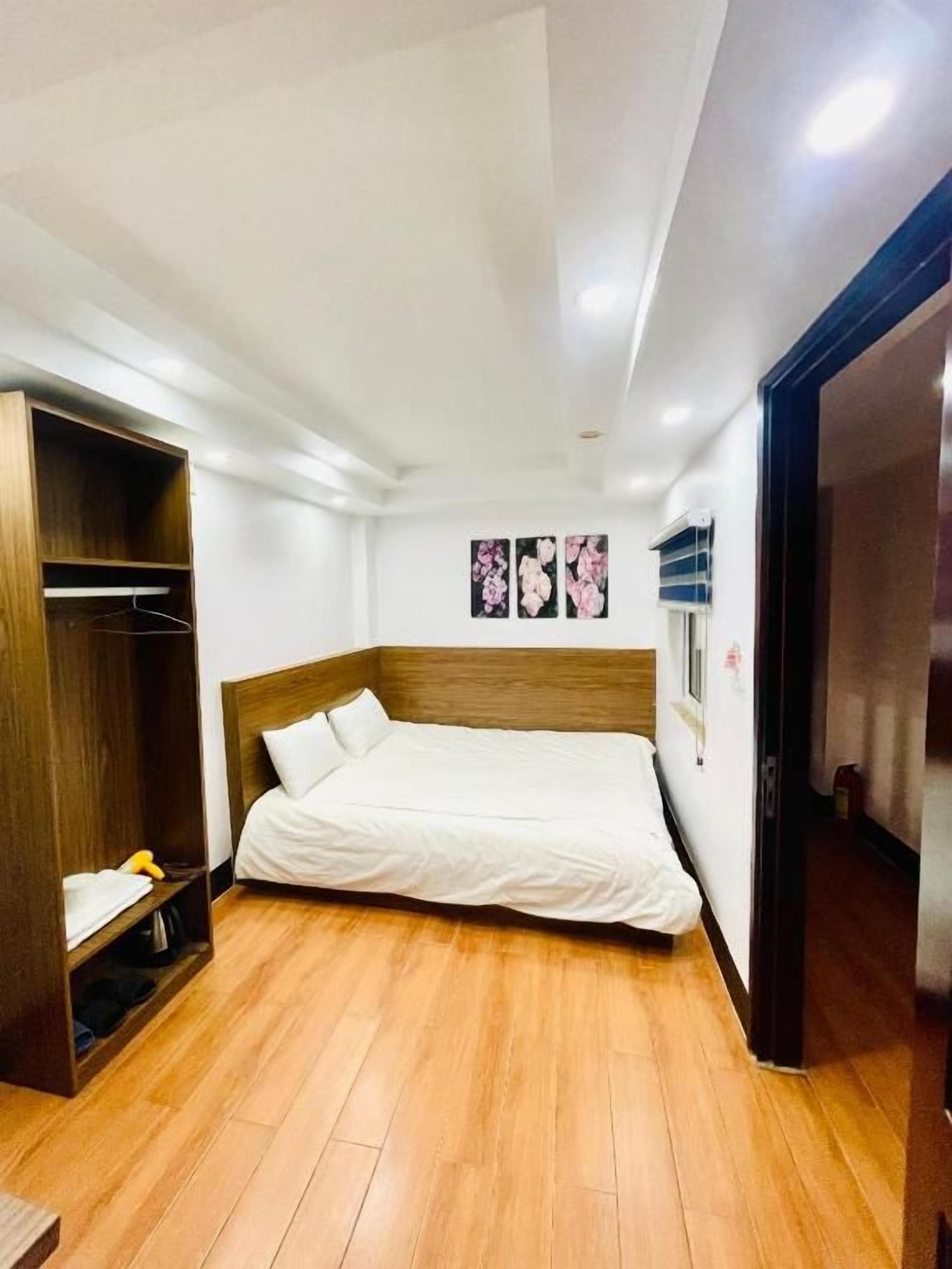 Un dormitorio con piso de madera, una cama con ropa de cama blanca, un armario de madera y un equipo de aire acondicionado instalado en la pared.