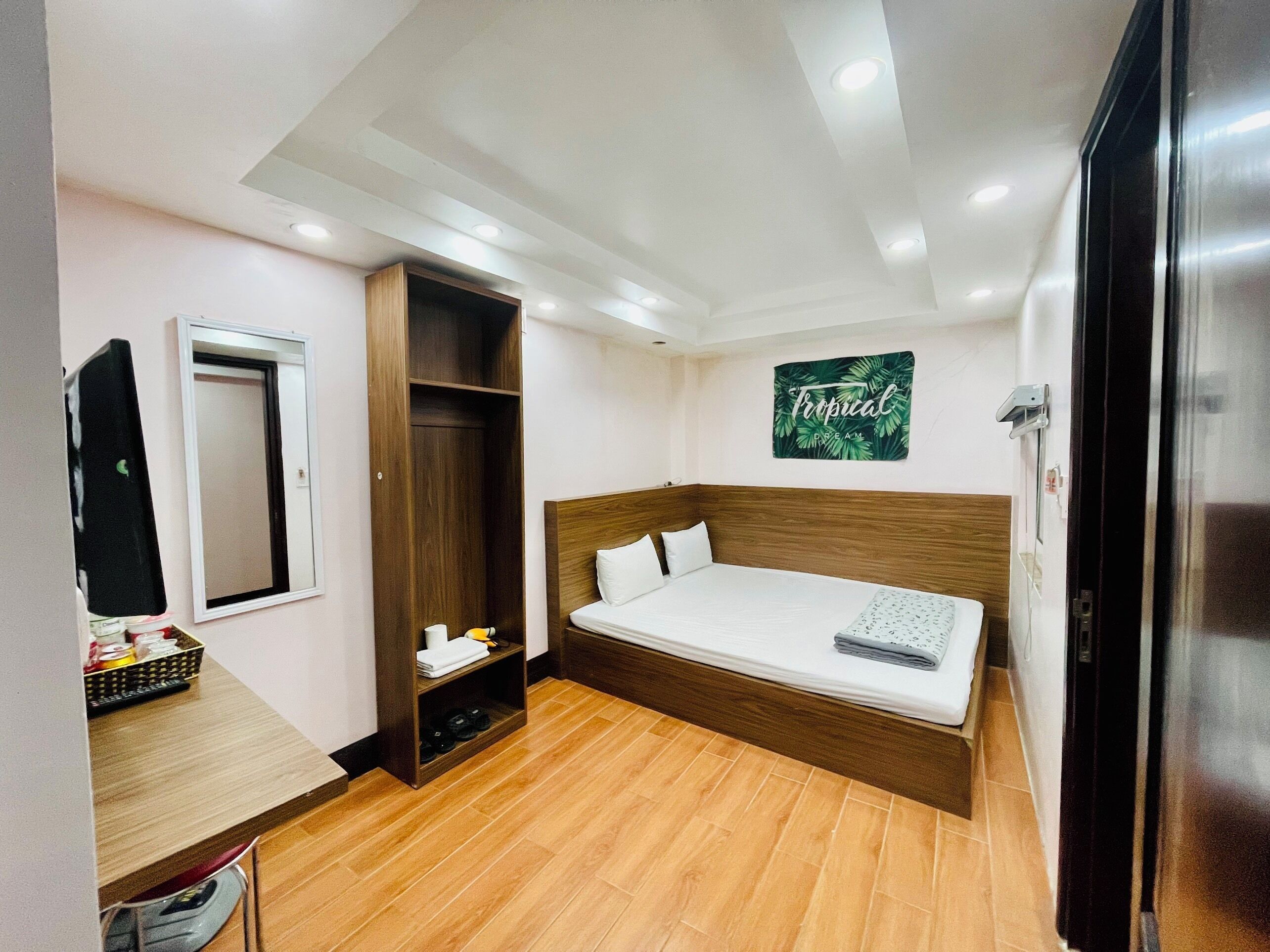 Una habitación de hotel compacta con una cama, un armario, un escritorio pequeño y un espejo.