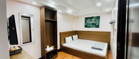 A compact hotel room with a bed, a wardrobe, a small desk, and a mirror.