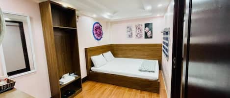 A bedroom with a bed, a wardrobe, a small table, and a refrigerator.