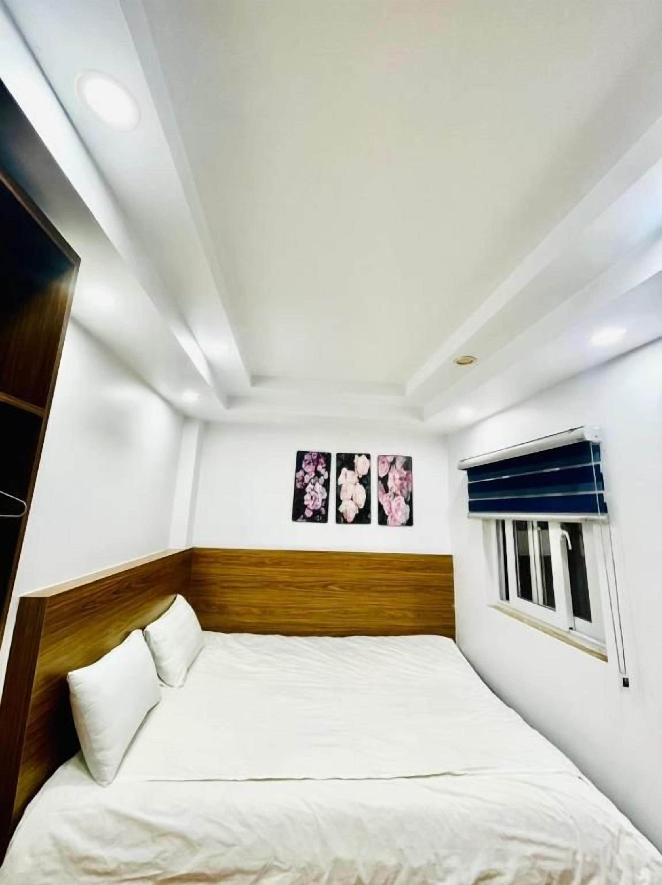 A bedroom with a bed, a wooden headboard, a window with blinds, and wall-mounted artwork.