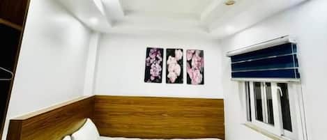 A bedroom with a bed, a wooden headboard, a window with blinds, and wall-mounted artwork.