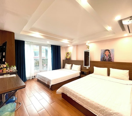 A hotel room with two beds, a desk, a chair, a TV, and a window with curtains.