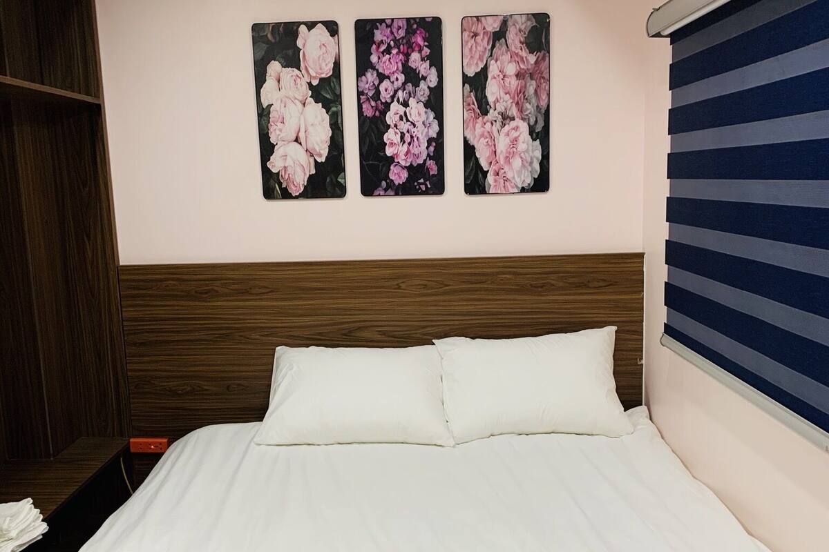 Quarto com cama, cabeceira de madeira e três quadros florais.