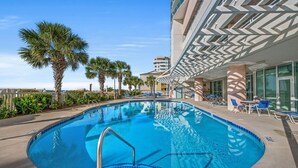 A swimming pool with a poolside area, palm trees, and a building with a modern design.