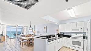 A modern kitchen with white cabinets, a central island, and a view of the sea.