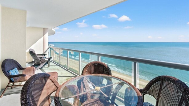 A balcony with wicker furniture, a glass table, and a view of the ocean.