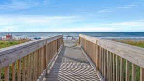 A wooden boardwalk leading to a beach with a lifeguard tower visible in the distance.