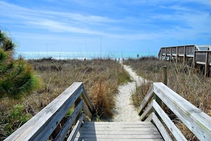 A wooden boardwalk leading to a beach with a fence and a wooden structure in the background.