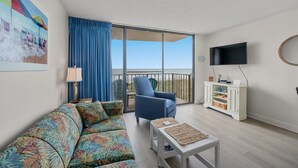 A living room with a sofa, armchair, and coffee table, a TV, and a balcony with a view. - Fantastic views from this 1-bedroom oceanfront condo in Carolina Reef! | Carolina Reef -  105 (North Myrtle Beach)