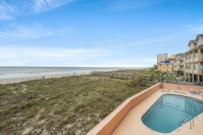 A beachfront view with a pool area, a beach, and a building with multiple balconies.