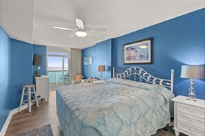 A bedroom with a bed, a desk, a chair, a balcony with a view, and a ceiling fan. - Bright beautiful 2 bedroom condo on the beach! | Crescent Keyes -  703 (North Myrtle Beach)