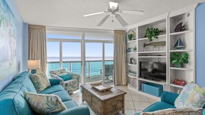 A living room with a view of the ocean, a ceiling fan, and a bookshelf with various items. - Bright beautiful 2 bedroom condo on the beach! | Crescent Keyes -  703 (North Myrtle Beach)