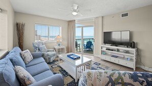 A living room with a sofa, coffee table, TV, and a balcony with ocean view. - This is a perfect 2-bedroom condo for a vacation at the seaside! | Crescent Keyes -  901 (North Myrtle Beach)