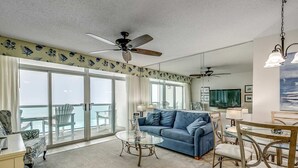 A spacious living room with a large blue sofa, a glass coffee table, and a ceiling fan. - Well planned and surprisingly spacious one bedroom! | Crescent Keyes -  907 (North Myrtle Beach)