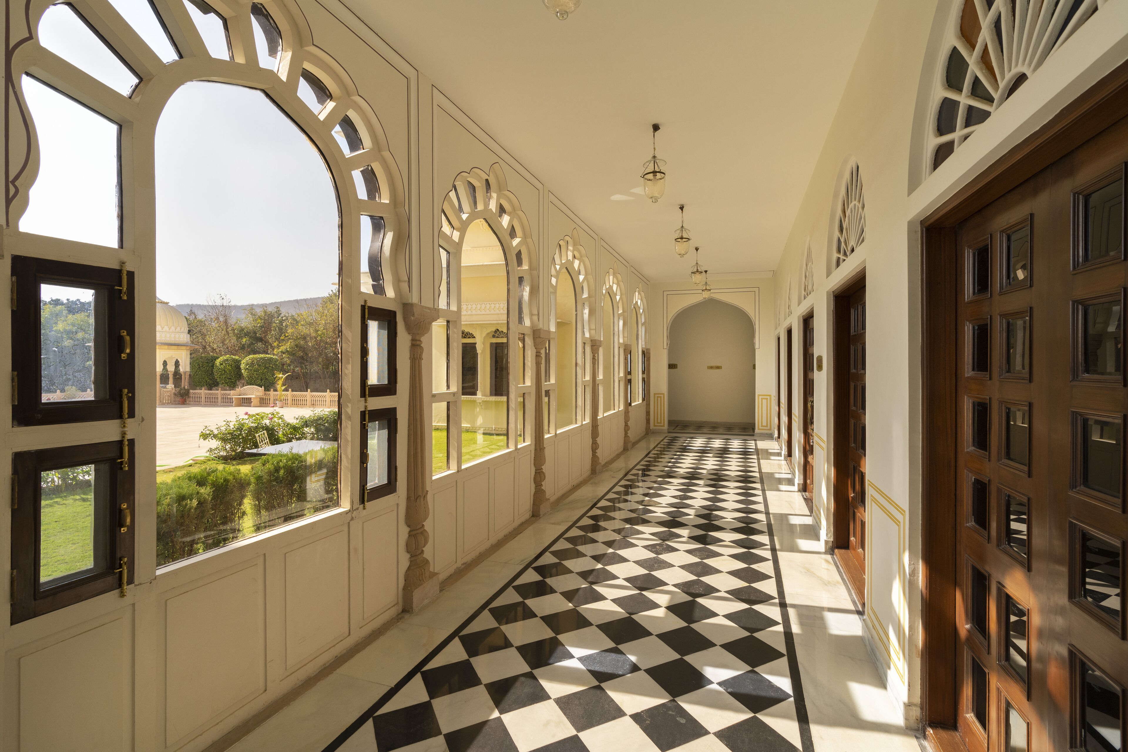 A corridor with a checkered floor, arched windows, and a view of a garden.