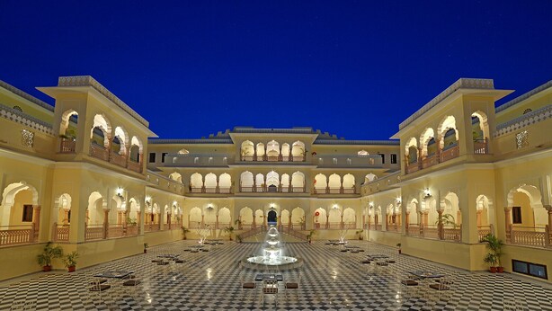 A spacious courtyard with a central fountain, surrounded by multiple balconies and arches, featuring a checkered floor pattern. - The Jaibagh Palace (Amer)