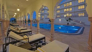A luxurious indoor pool area with multiple lounge chairs and a large pool. - The Jaibagh Palace (Amer)
