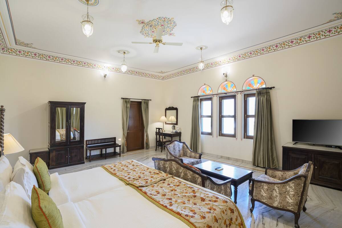 A hotel room with a large bed, two armchairs, a desk, a television, and a wardrobe.