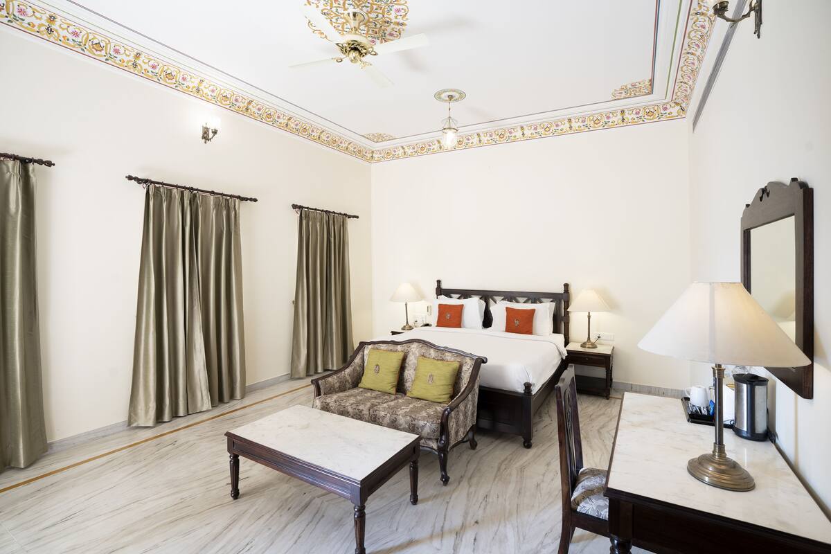 A hotel room with a bed, a sofa, a desk, and a ceiling fan.