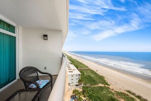 A balcony with a wicker chair, a small pool, and a view of the beach and ocean.