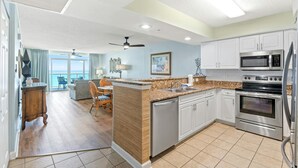 A modern kitchen with a central island, stainless steel appliances, and a view to the outside. - The stunning view is king in this Crescent Keyes oceanfront condo! | Crescent Keyes - 1008 (North Myrtle Beach)