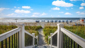 A beach view with a pathway leading to the beach, umbrellas, and a lifeguard tower. - The stunning view is king in this Crescent Keyes oceanfront condo! | Crescent Keyes - 1008 (North Myrtle Beach)