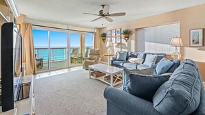 A living room with a large sofa, a coffee table, and a TV. There is a balcony with a view of the ocean. - Beautiful 3 bedroom condo with a great oceanfront view! | Crescent Keyes -  710 (North Myrtle Beach)