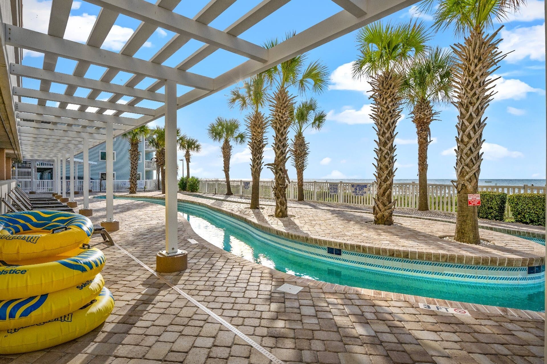 A pool area with a clear view of the ocean, palm trees, and a covered walkway.
