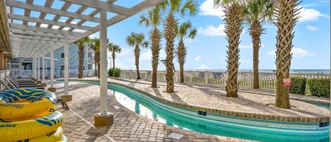 A pool area with a clear view of the ocean, palm trees, and a covered walkway.