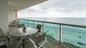 A balcony with a round table and chairs, overlooking a beach with people and boats. - Ultra stylish 3-bedroom 3-bathroom oceanfront condo | Crescent Keyes - 908 (North Myrtle Beach)