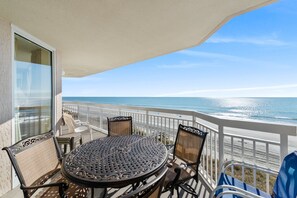 A balcony with a table and chairs, overlooking a beach.