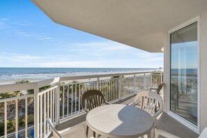 Ein Balkon mit Blick auf den Strand, ein Tisch und zwei Stühle.