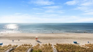 Ein Strand mit blauem Himmel, einem Rettungsturm und einer Holzpromenade, die zum Wasser führt.