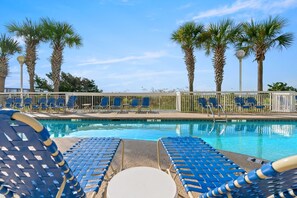Un espace aménagé au bord de la piscine, avec des chaises longues bleues et des palmiers.