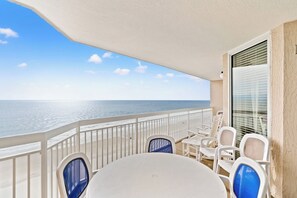 Un balcon avec vue sur l’océan, des chaises blanches et une table.