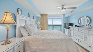 Un dormitorio con cama, televisor, cómoda y vista al océano.