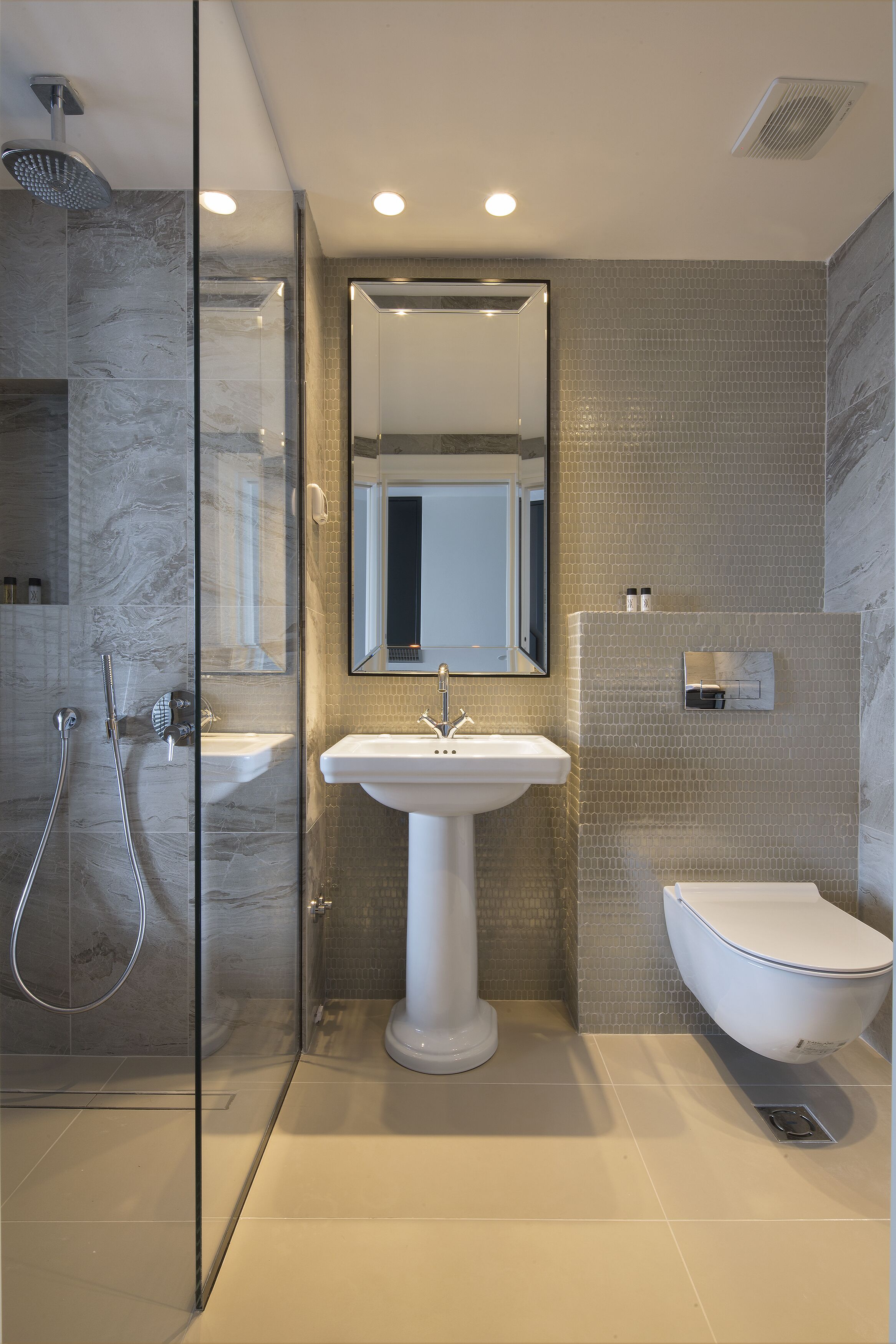A modern bathroom with a glass-enclosed shower, a pedestal sink, and a toilet.