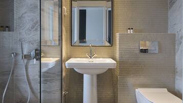 A modern bathroom with a glass-enclosed shower, a pedestal sink, and a toilet.