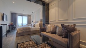 A modern hotel room with a large bed, a sofa, a glass coffee table, and a view of the sea. - Vivid Blue Serenity Resort (Petrovac)