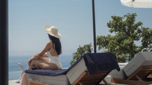 A woman sitting on a lounge chair under a white umbrella, overlooking a body of water. - Vivid Blue Serenity Resort (Petrovac)