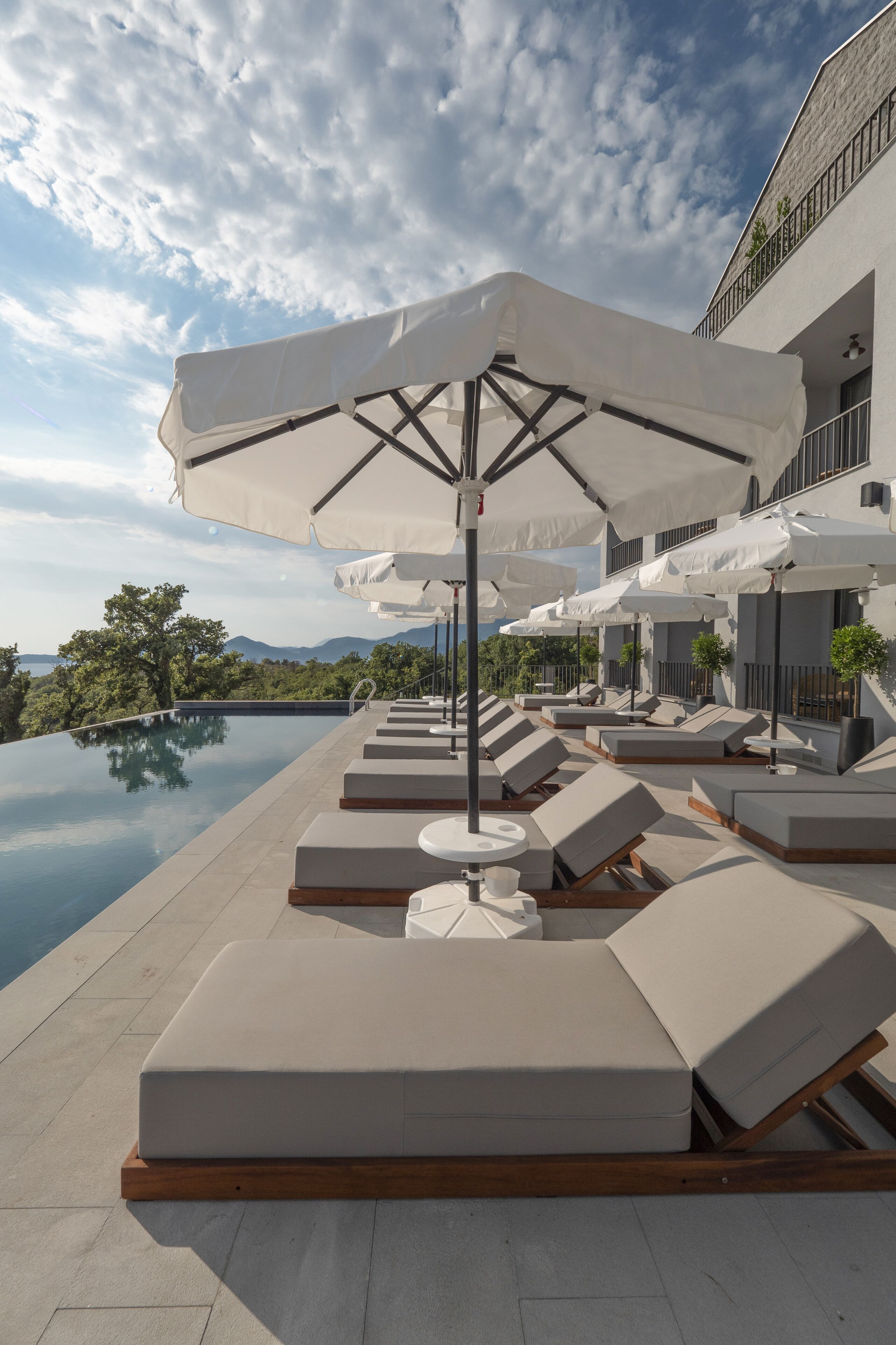 Piscina infinita en la azotea con sillones de descanso y sombrillas, con vistas a un paisaje montañoso.