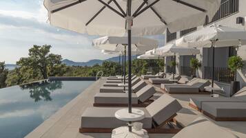 Piscina infinita en la azotea con sillones de descanso y sombrillas, con vistas a un paisaje montañoso.